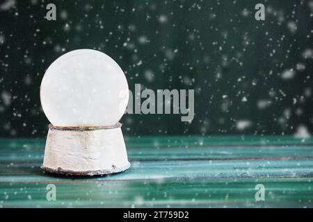 Magische leere Schneekugel über einem grünen rustikalen Tischhintergrund mit fallendem Schnee. Verschwommener Vorder- und Hintergrund. Kopierbereich verfügbar. Stockfoto