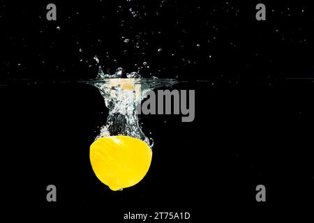 Halbierte Zitrone fällt sauberes Wasser vor schwarzem Hintergrund Stockfoto