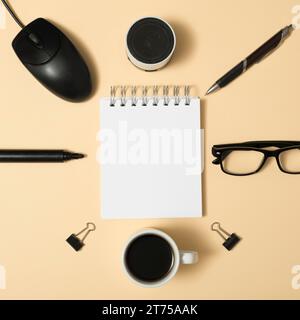 Hohe Winkelansicht leerer Spiralnotizblock umgeben von bluetooth Lautsprecher Stift Büroklammern Kaffeetasse Brille beige Hintergrund Stockfoto