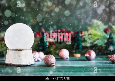 Magische leere Schneekugel über einem grünen rustikalen Tischhintergrund mit fallendem Schnee. Weihnachtsdekoration im Hintergrund. Unscharfer Hintergrund. Stockfoto