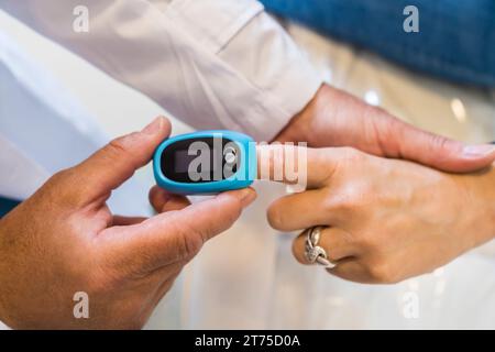 Der Arzt legt seinem Patienten ein Pulsoxymeter in die Hand, um die Sauerstoffsättigung im Blut und die Herzfrequenz zu messen. Stockfoto