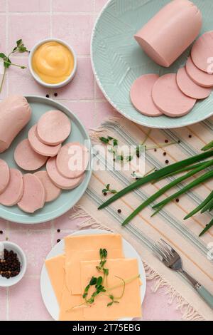 Zusammensetzung mit gekochter Wurst auf dem Teller, grünen Zwiebeln und Sauce auf einem rosa Fliesentisch Stockfoto