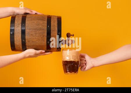 Frau, die Bier aus dem Fass in einen Becher auf gelbem Hintergrund gießt Stockfoto