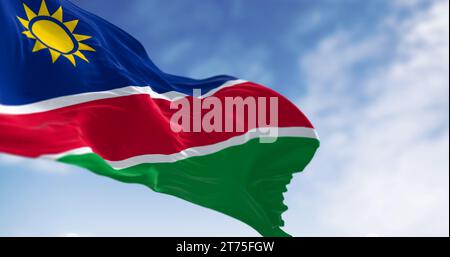Namibische Nationalflagge winkt an einem klaren Tag. Blaue Streifen, gelbe Sonne, rote, weiße Streifen, grün. Ovambo-Farbe. 3D-Darstellung. Selektiver Fokus Stockfoto