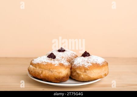 Teller mit leckeren Donuts für die Hanukkah-Feier auf Holztisch vor farbigem Hintergrund Stockfoto