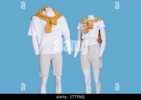 Weibliche und männliche Schaufensterpuppen in weißen T-Shirts, stylischen Shorts und orangefarbenen Pullover auf hellblauem Hintergrund Stockfoto
