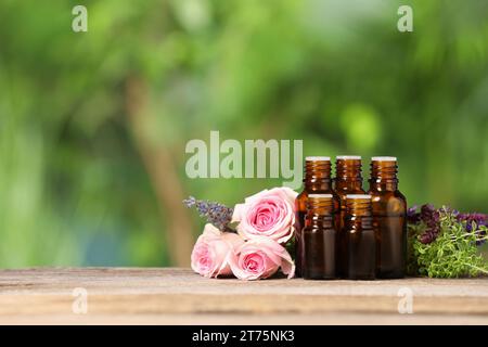 Flaschen mit ätherischen Ölen, Kräutern und Blumen auf Holztisch vor verschwommenem grünem Hintergrund. Leerzeichen für Text Stockfoto