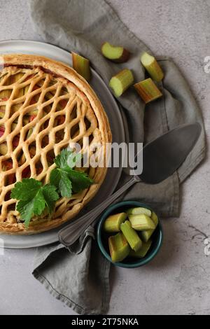 Frisch gebackener Rhabarberkuchen, geschnittene Stängel und Kuchenservice auf hellgrauem Tisch, flach liegend Stockfoto