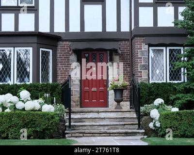 Die Eingangstür des traditionellen, zweistöckigen Hauses im Tudor-Stil mit Hortensie-Büschen in Blüte Stockfoto