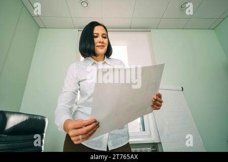 Porträt einer jungen Geschäftsfrau, die sich Karten ansieht und Gewinne mit Vertrauen im Büro plant Stockfoto