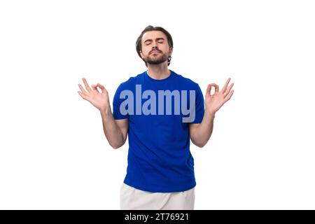 Junger brünette Mann mit Bart in einem blauen T-Shirt meditiert auf weißem Hintergrund Stockfoto