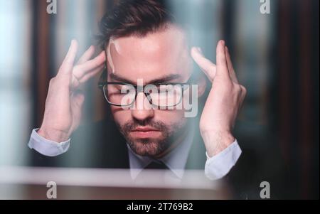 Müde, erschöpfter Mann, Büroangestellter, Manager oder Freiberufler, der an seinem Schreibtisch sitzt und es satt hat, in einem Laptop zu arbeiten Stockfoto