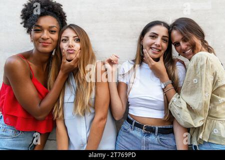 Vier lächelnde Freunde, die Spaß daran haben, alberne Gesichter gegen eine helle Wand zu machen. Stockfoto