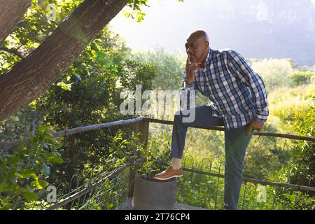 Nachdenklicher afroamerikaner, der auf einem Zaun im sonnigen Garten sitzt, Kopierraum Stockfoto