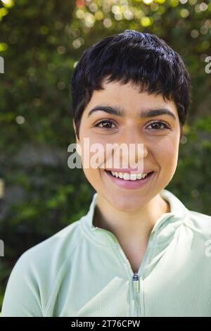 Porträt einer glücklichen birassischen Frau mit kurzen dunklen Haaren, die im sonnigen Garten lächelt Stockfoto