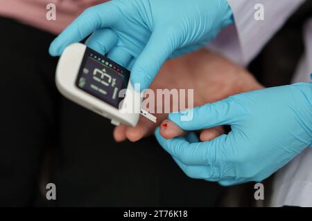 Schließen Sie einen Arzt mit Glukometer auf, der den Blutzuckerspiegel einer älteren Frau überprüft. Check Diabetes Konzept Stockfoto