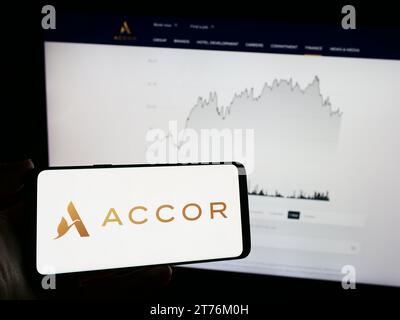 Person, die ein Mobiltelefon mit dem Logo des französischen Hotelunternehmens Accor SA vor der Business-Webseite hält. Schwerpunkt auf dem Display des Telefons. Stockfoto
