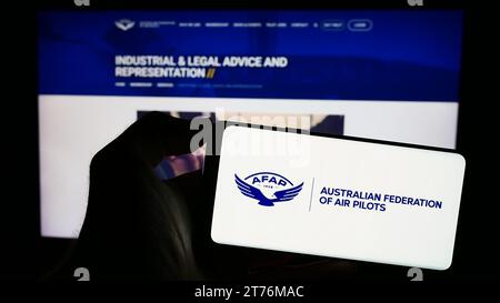 Person, die ein Mobiltelefon mit dem Logo des Verbands Australian Federation of Air Pilots (AFAP) vor der Webseite hält. Schwerpunkt auf dem Display des Telefons. Stockfoto