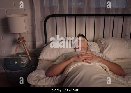 Eine junge Frau liegt bequem auf ihrem Bauch in einem gemütlichen Bett, weiße Laken leicht um sie gelegt Stockfoto