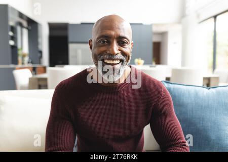 Glücklicher afroamerikaner reifer Mann, der Videoanrufe hat und im sonnigen Wohnzimmer zu Hause lächelt Stockfoto