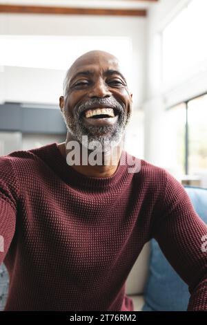 Glücklicher afroamerikaner reifer Mann, der Videoanruf hat und im sonnigen Wohnzimmer zu Hause lacht Stockfoto