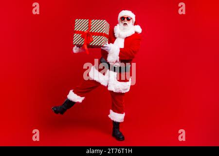 Großes Porträt der überglücklich positiven weihnachtsmann Hände halten Neujahrsgeschenkkasten isoliert auf leuchtendem rotem Hintergrund Stockfoto