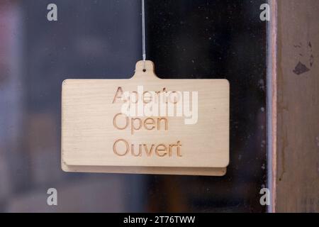 Weißes Schild, das an der Glastür eines Ladens hängt und auf Italienisch, Englisch und Französisch steht: "Offen". Stockfoto