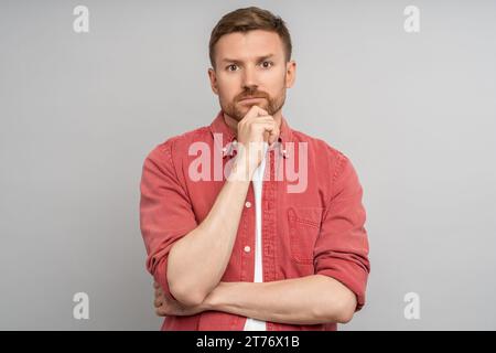 Ernsthafter Mann, der das Kinn hält, nachdenkt, unzufrieden, enttäuscht, Emotionen, Studiohintergrund Stockfoto