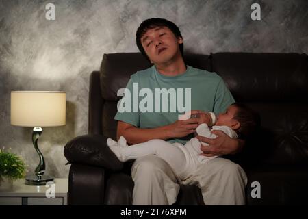 Schläfriger und müder Vater füttert das Baby nachts auf einem Sofa im Wohnzimmer mit einer Milchflasche Stockfoto