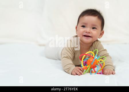 Kleinkind spielt mit bunten Gummibissen Spielzeug auf einem Bett Stockfoto