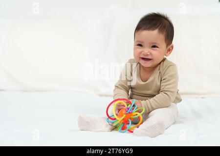 Kleinkind spielt mit bunten Gummibissen Spielzeug auf einem Bett Stockfoto