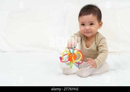 Kleinkind spielt mit bunten Gummibissen Spielzeug auf einem Bett Stockfoto