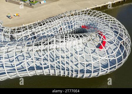 Moderne, geschwungene Fußbrücke aus Stahlband aus der Vogelperspektive in den Docklands in Melbourne, Victoria, Australien. Stockfoto