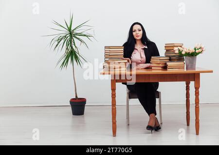 Eine Frau in der Bibliothek sitzt an einem Tisch mit einem Stapel Bücher Stockfoto