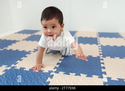 Glückliches Baby, das auf Spielmatte oder Puzzle-Boden krabbelt Stockfoto