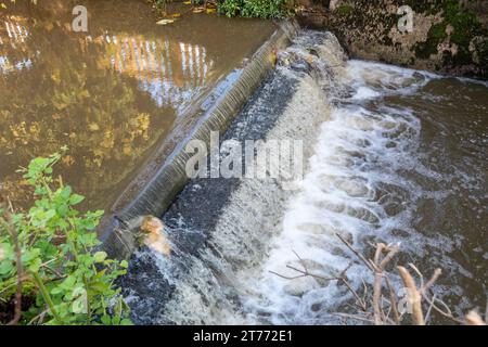 Ein kleiner Wasserfall über einem Wehr am Ende einer Schlammfalle. Stockfoto