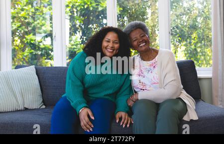 Ältere glückliche afroamerikanische Mutter und erwachsene Tochter, die zu Hause auf der Couch sitzen, Kopierraum Stockfoto