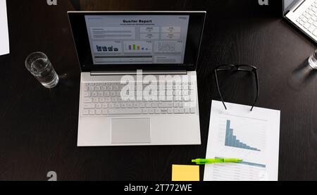 Laptop mit Quartalsbericht und Diagrammen auf dem Bildschirm und Dokument auf dem Tisch im Besprechungsraum Stockfoto