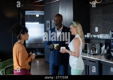 Glückliche, vielfältige männliche und weibliche Kollegen, die Kaffee trinken und sich im Stehen in der Cafeteria unterhalten Stockfoto