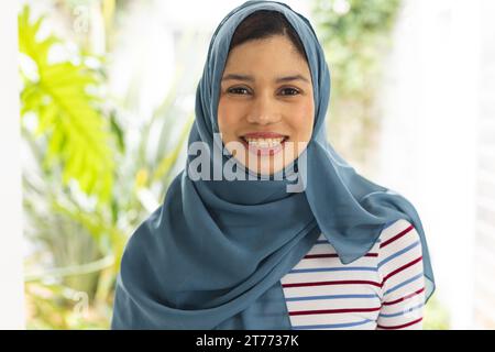 Porträt einer glücklichen birassischen Frau im Hijab im sonnigen Haus Stockfoto