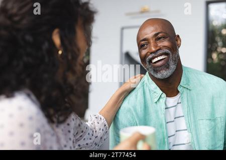 Glückliches reifes, vielseitiges Paar, das Kaffee trinkt und sich in der Küche unterhalten kann Stockfoto