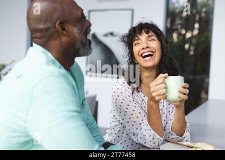 Glückliches reifes, vielseitiges Paar, das Kaffee trinkt und in der Küche lacht Stockfoto