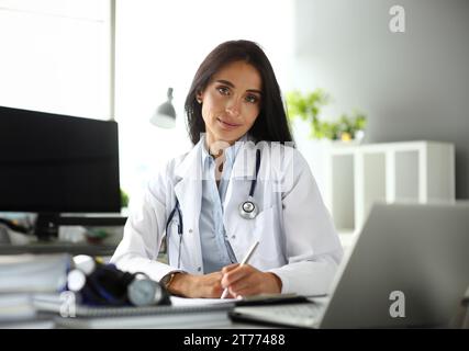 Hübsche reife weibliche GP am Arbeitstisch Notizen zu machen Stockfoto