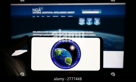 Person, die ein Smartphone mit dem Siegel der US National Geospatial-Intelligence Agency (NGA) vor der Website hält. Schwerpunkt auf dem Display des Telefons. Stockfoto