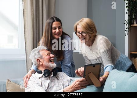 Familientreffen. Vater, Mutter und Tochter im Familienhaus erinnern sich an die Vergangenheit, indem sie alte Fotos aus ihrer Jugend anschauen. Nostalgie und ha Stockfoto