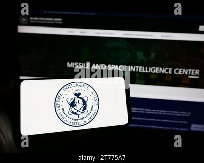 Person, die vor der Webseite ein Mobiltelefon mit dem Siegel der United States Defense Intelligence Agency (DIA) hält. Schwerpunkt auf dem Display des Telefons. Stockfoto