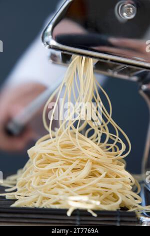 Haufen von frische Tagliolini kommen aus einer Nudelmaschine mit der Hand drehen am Griff Stockfoto