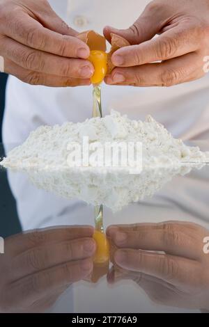 Nahaufnahme einer Koch-Hände bricht ein Ei über ein Haufen Mehl über einen Glastisch Stockfoto