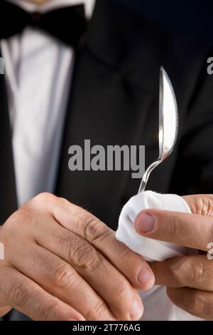 Nahaufnahme eines Kellners, der einen silbernen Löffel mit einer weißen Serviette poliert Stockfoto