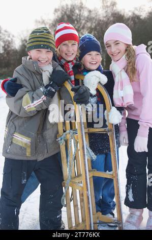 Lächelnde Kinder, die sich auf einen Schlitten lehnen Stockfoto